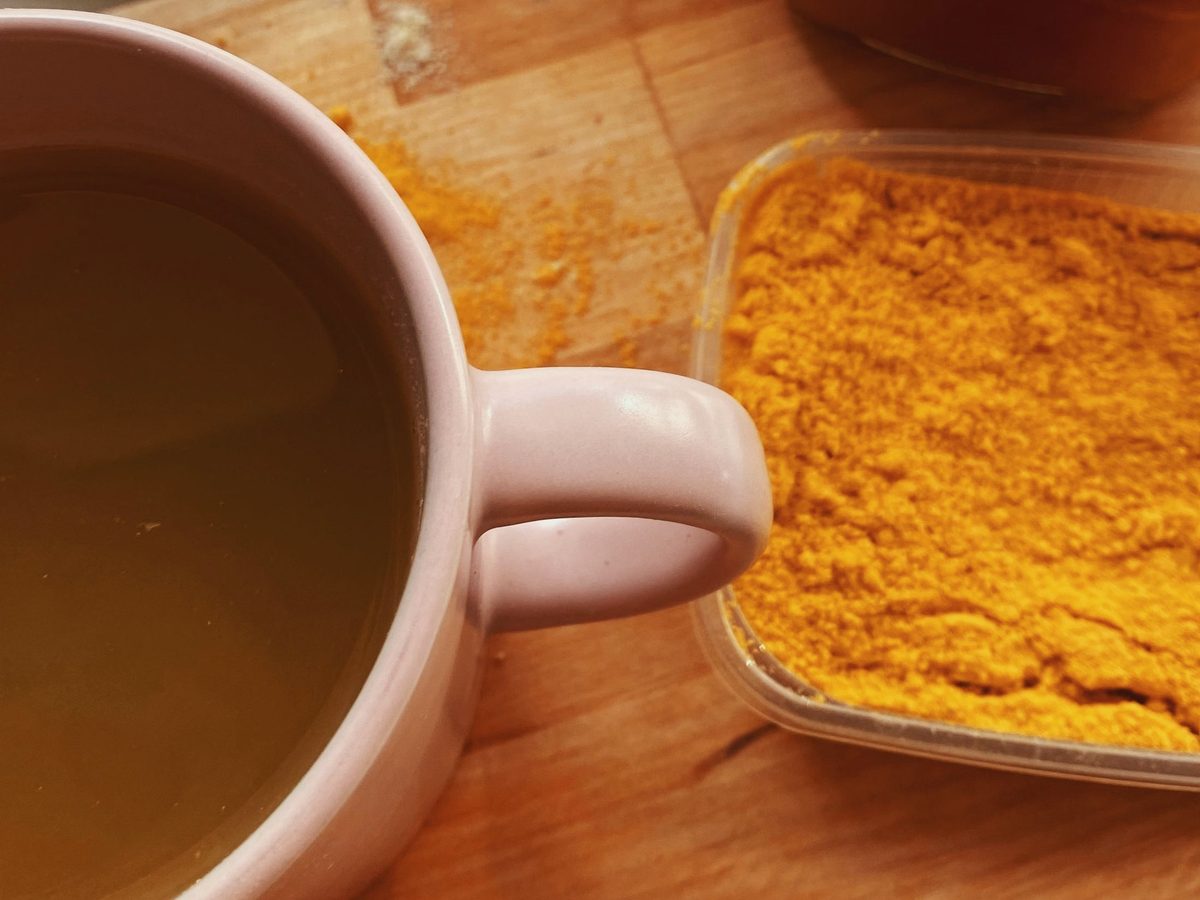 A turmeric drink beside a tray of ground turmeric