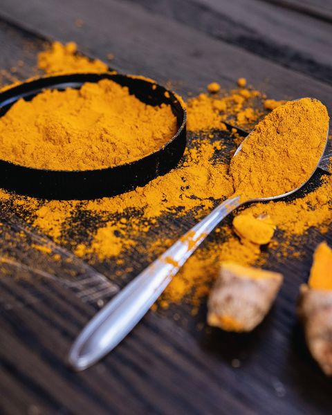 Ground turmeric in a dark dish with a spoon and dried turmeric root