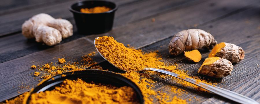 Ground turmeric beside dried turmeric and ginger root